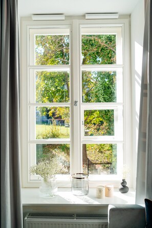 A window with a view of trees and a garden. There are two candles and a vase on the windowsill. - Warsaw Story by StayLab (Warsaw)
