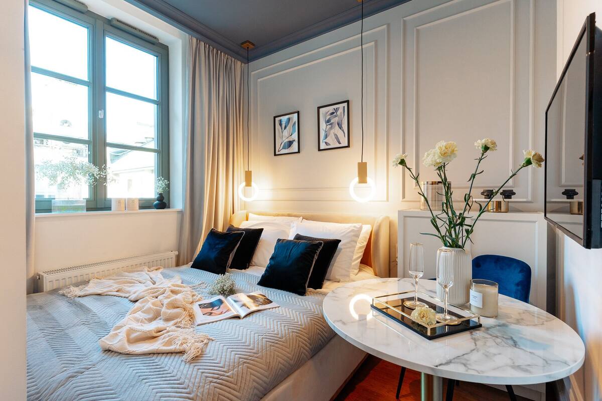 Una habitación de hotel moderna con una cama grande, una mesita de noche y un comedor con una mesa de mármol.