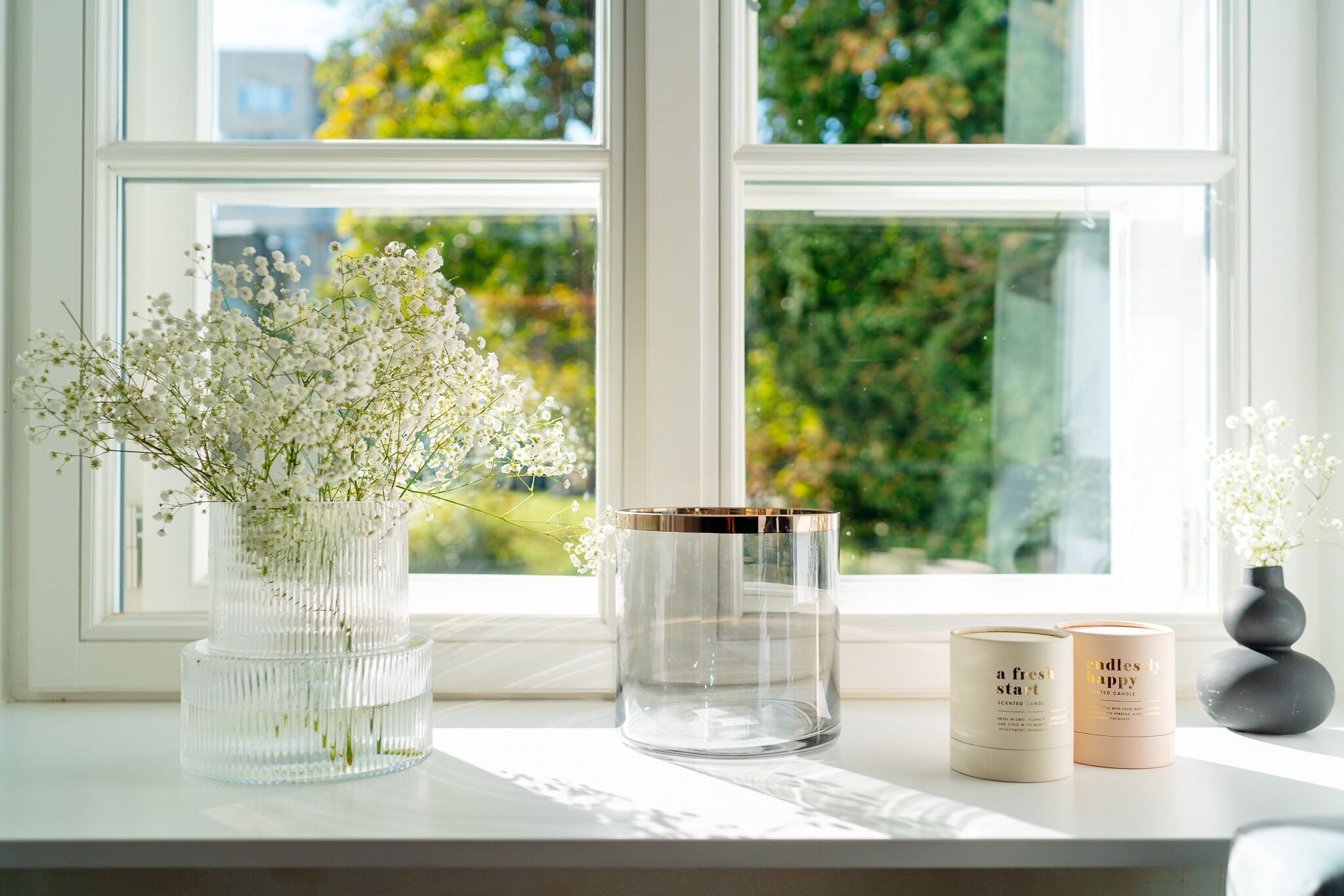 Une fenêtre avec deux bougies et un vase de fleurs posé sur le rebord.
