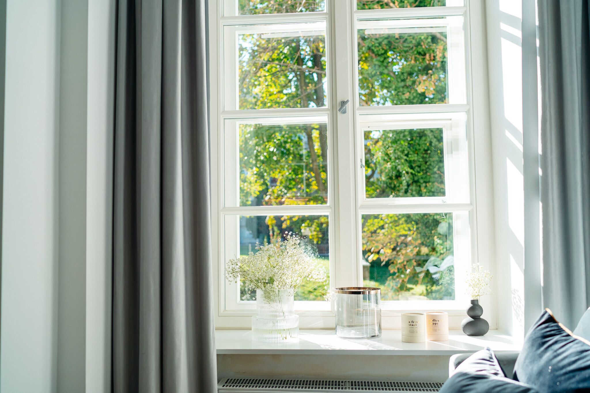Una ventana con vistas a la vegetación, un florero con flores y velas en el alféizar.