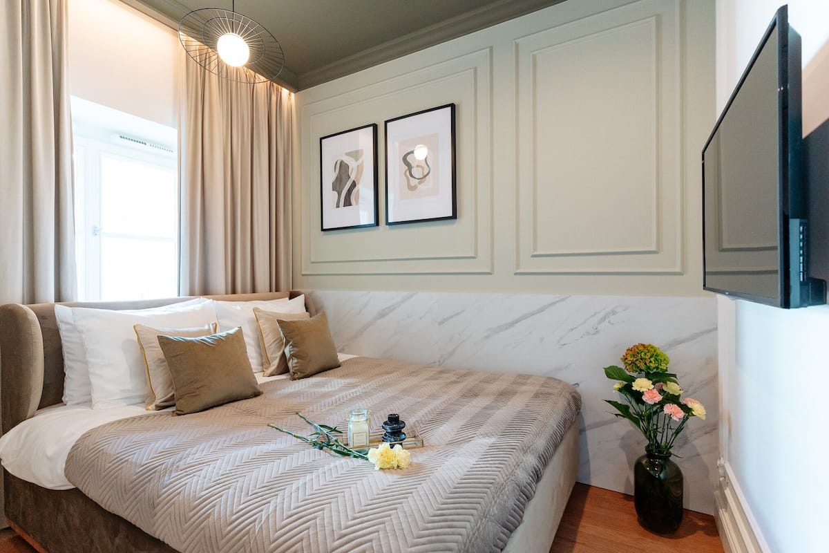 Una cama bien hecha con una colcha estampada, un florero con flores y un cuadro en la pared.