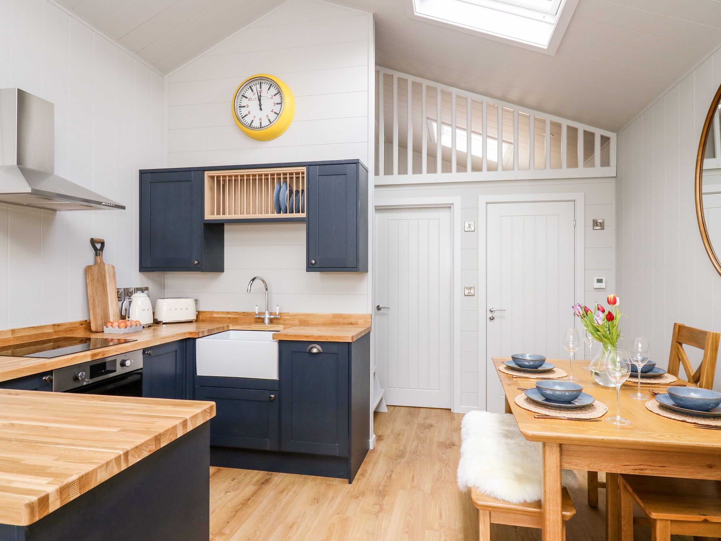 A modern kitchen with dark cabinets, a wooden countertop, a built-in oven, and a skylight.