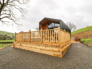 Une terrasse en bois avec une rambarde, un bâtiment moderne à la façade sombre et un sol recouvert de gravier.