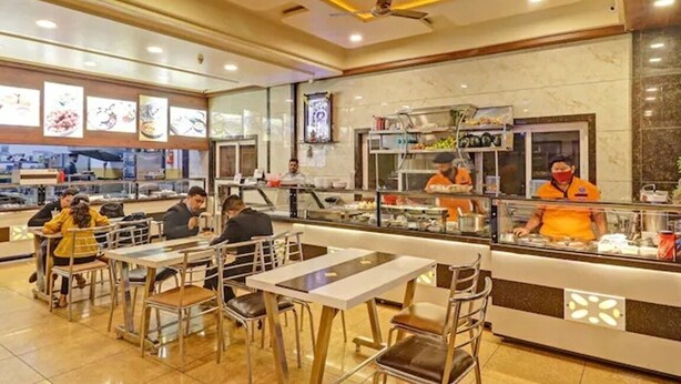 Un ristorante con un bancone, una sala con posti a sedere e personale.