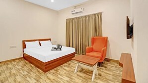 Una camera d'albergo con un letto in legno, un tavolino, una sedia arancione e una TV montata a parete.