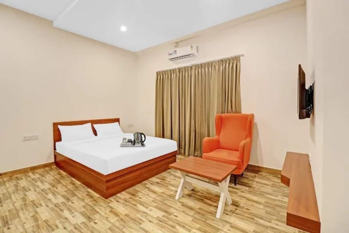A hotel room with a wooden bed, a small table, an orange chair, and a TV mounted on the wall.