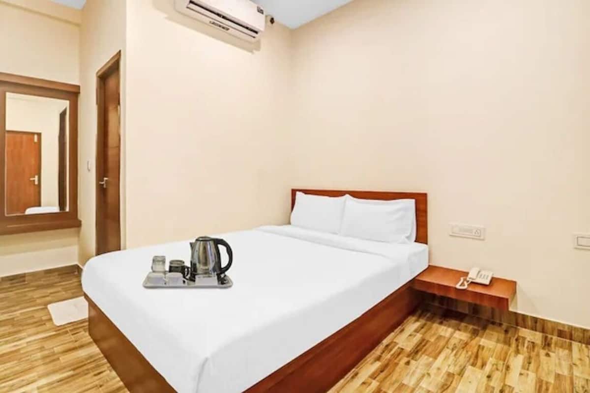 A hotel room with a bed, a bedside table with a phone, and a tray with a kettle and cups.