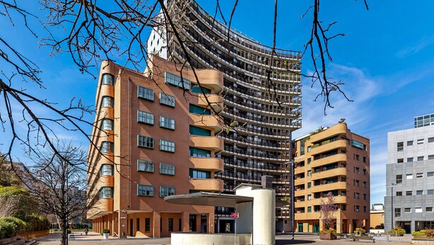 Un edificio moderno con fachada curva, varios balcones y un patio central con zona de estar.