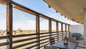 Un balcón con mesa y sillas, vistas a la ciudad y una barandilla.