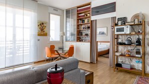 Una sala de estar moderna con un sofá gris, una tetera roja y una estantería llena de libros y objetos decorativos.