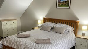 A neatly made bed with checkered bedding, two bedside tables with lamps, a wooden headboard, and a picture on the wall. - Till Cottage 3 Fenton Hill Farm (Wooler)