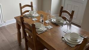 A wooden dining table set with white plates, bowls, and glasses, surrounded by wooden chairs. - Till Cottage 3 Fenton Hill Farm (Wooler)