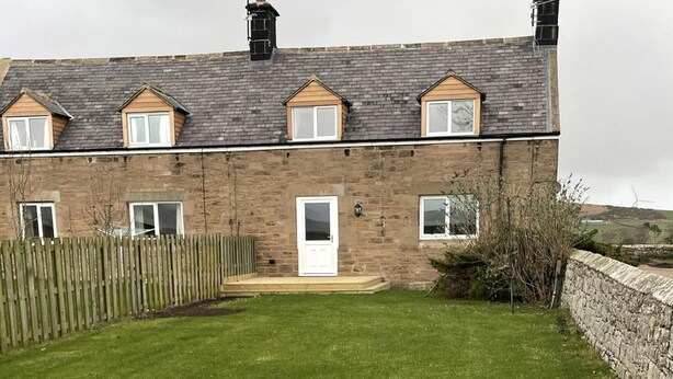 A two-story stone house with a front door, a small porch, and a fenced backyard. - Till Cottage 3 Fenton Hill Farm (Wooler)