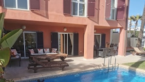 Ein Poolbereich mit Holzterrasse, Liegestühlen und einer Sitzgruppe mit Kissen.