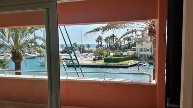 Ein Balkon mit Blick auf einen Yachthafen, Palmen und ein Gebäude mit weißer Fassade.