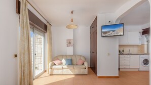 Una sala de estar con sofá, televisor y una zona de cocina con lavadora.