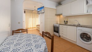 Una cocina compacta con armarios blancos, lavadora y horno pequeño.