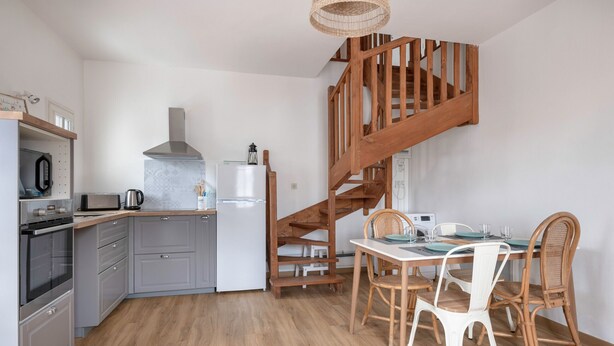 A modern kitchen with grey cabinets, a wooden staircase, and a dining area with white chairs and a table. - Family stay at 400m from the beach (Sarzeau)