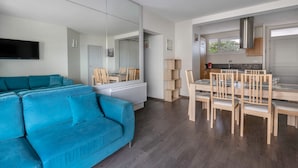 Una sala de estar moderna con un sofá azul, un comedor con mobiliario de madera y una cocina con campana extractora de acero inoxidable.