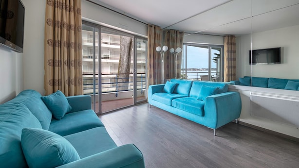 Una sala de estar moderna con un sofá azul, una mesita de centro y un amplio ventanal con vistas a un edificio.