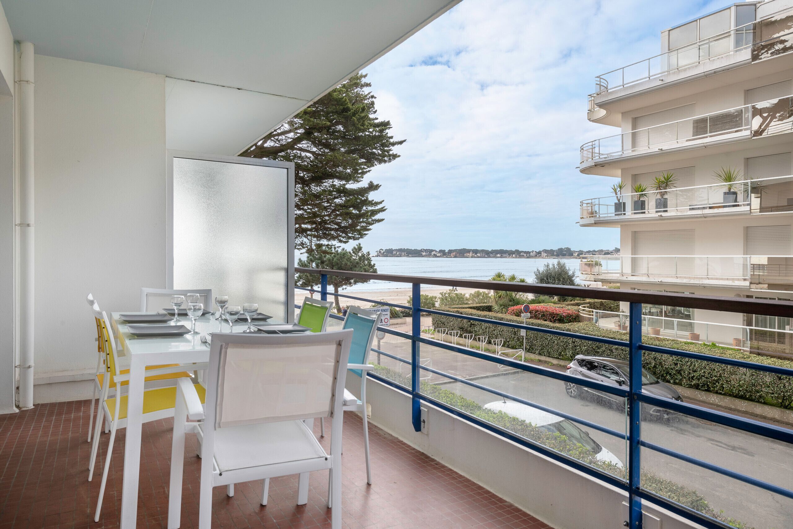 Ein Balkon mit Esstisch, gedeckt für vier Personen, mit Blick auf eine Küstenlandschaft und dem Meer sowie ein mehrstöckiges Gebäude.