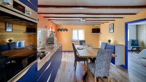 A modern kitchen with a built-in oven, a dining area with a wooden table and chairs, and a blue accent wall. - Duo vacation near the sea (Le Guilvinec)