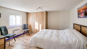 A bedroom with a large bed, two chairs, a window, a radiator, and a painting on the wall. - Duo vacation near the sea (Le Guilvinec)