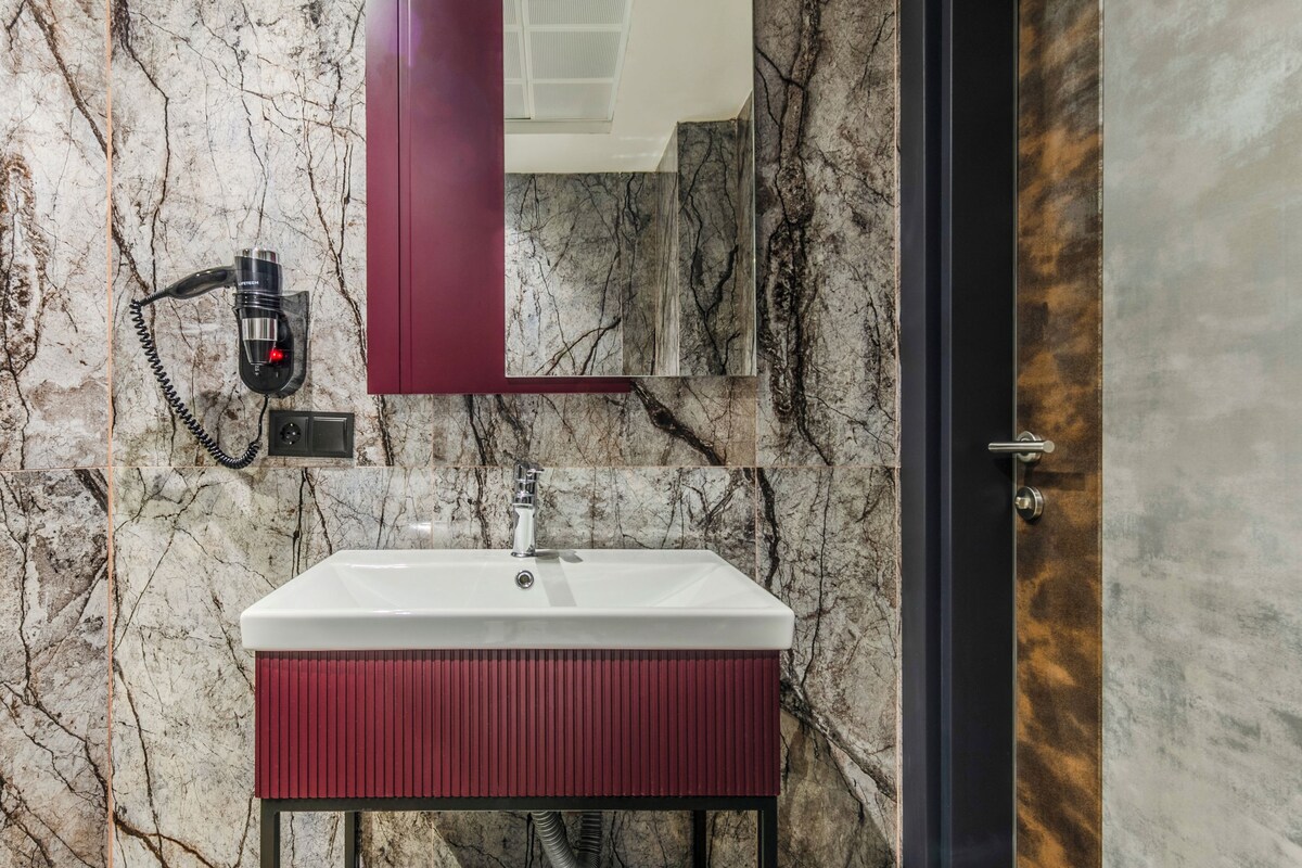 A bathroom with a marble wall, a white sink, a red vanity, and a towel rack.