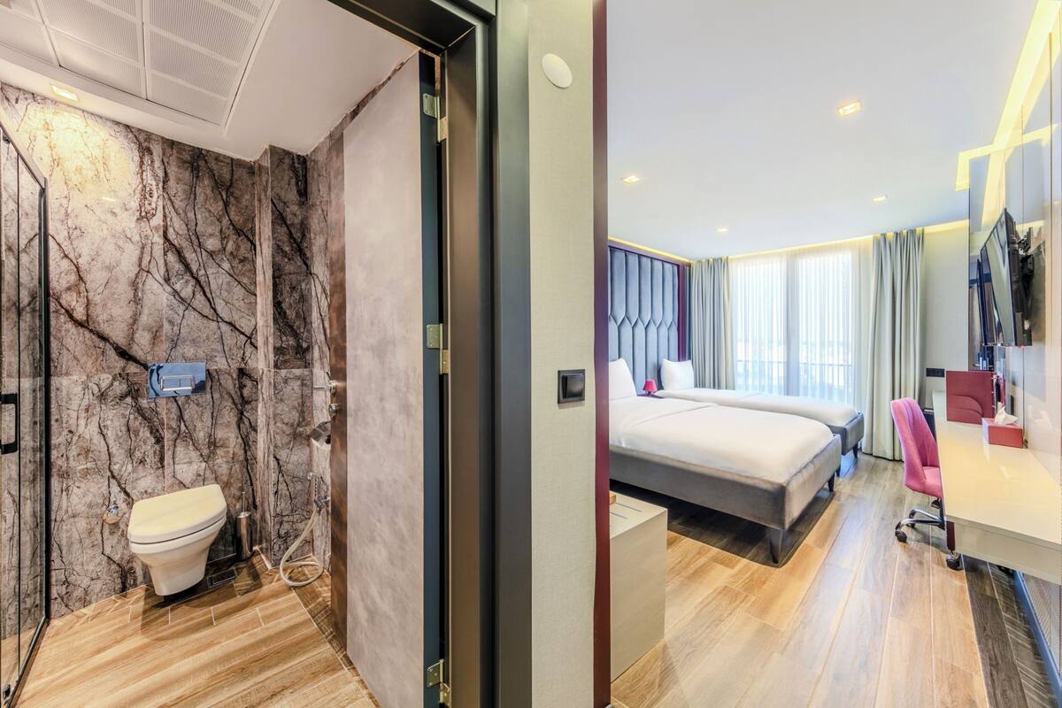 A modern hotel room with a marble bathroom, a bed with a large window, and a desk with a chair.