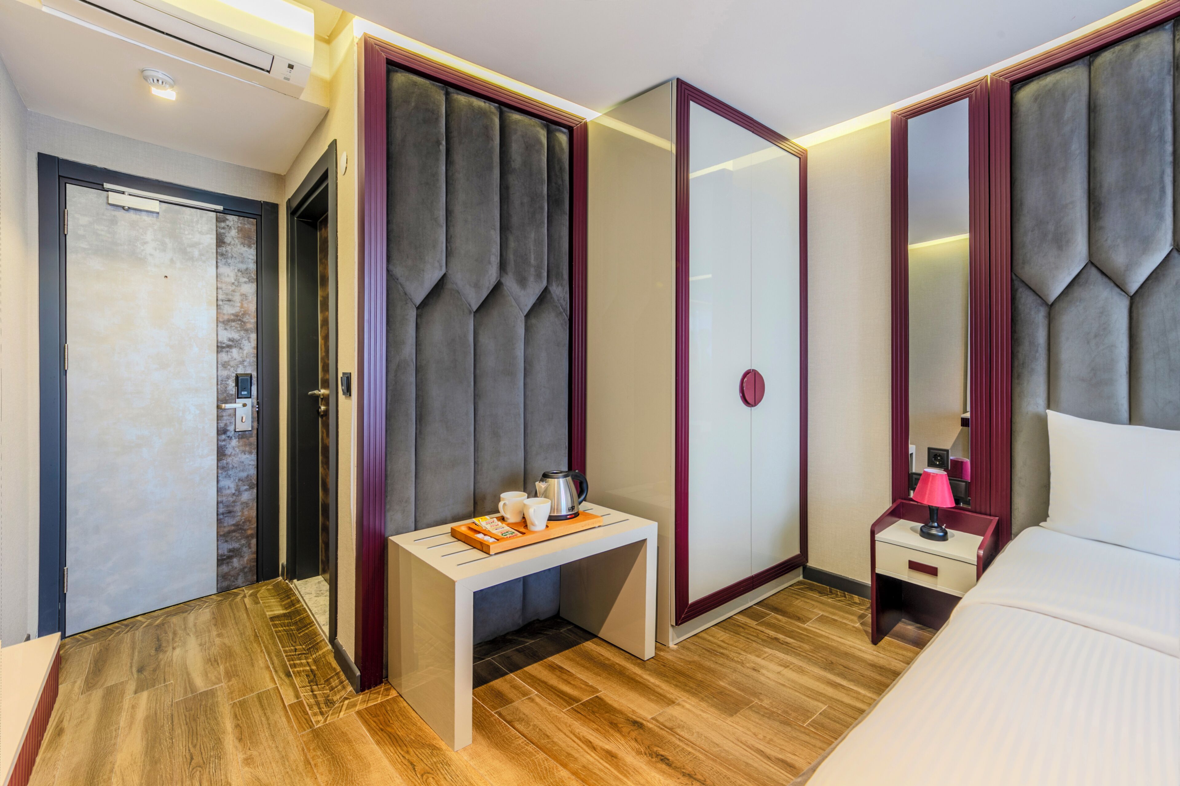 A hotel room with a bed, bedside table, nightstand, and a mirror.
