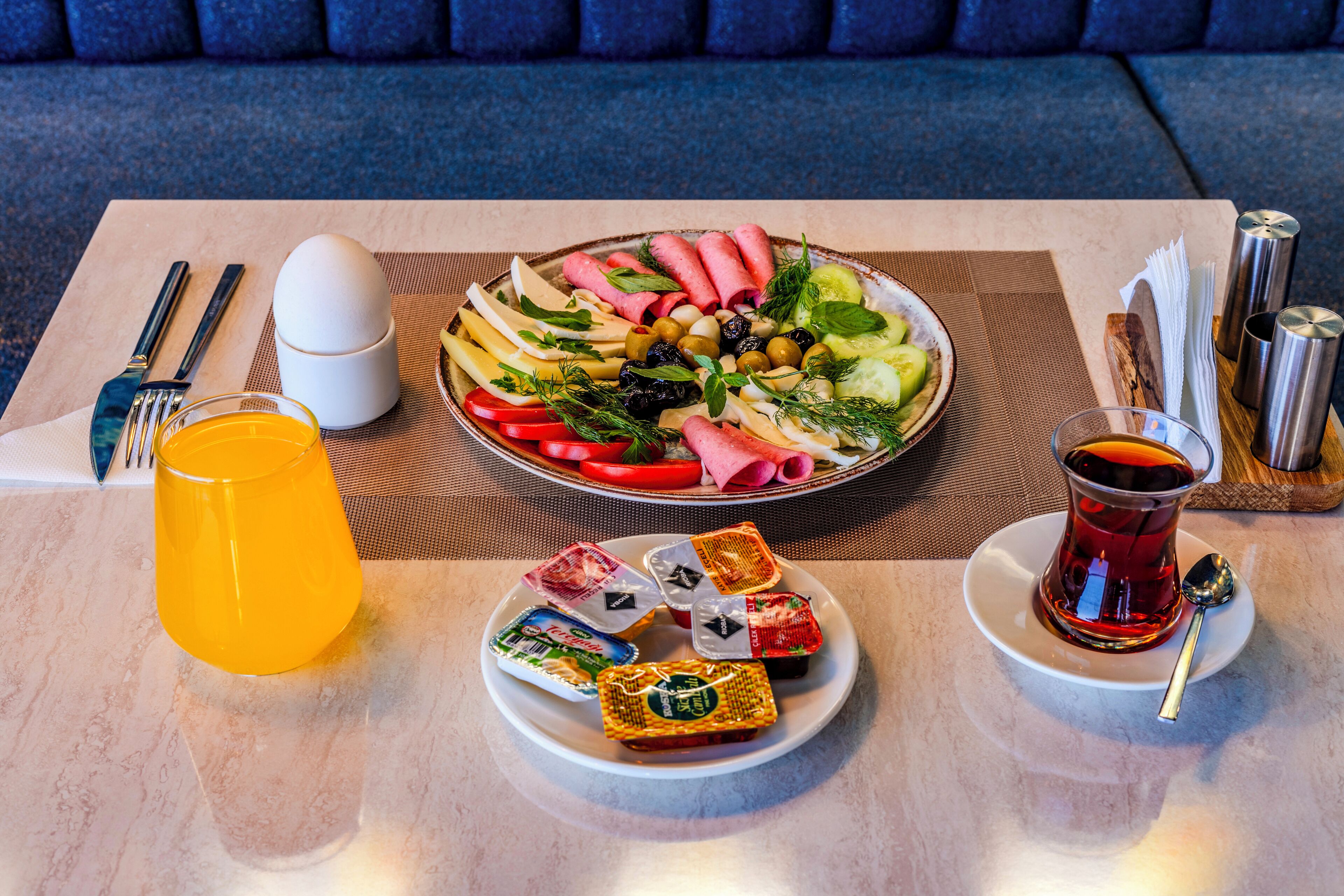 A table with a plate of food, a glass of orange juice, a cup of tea, and condiments.
