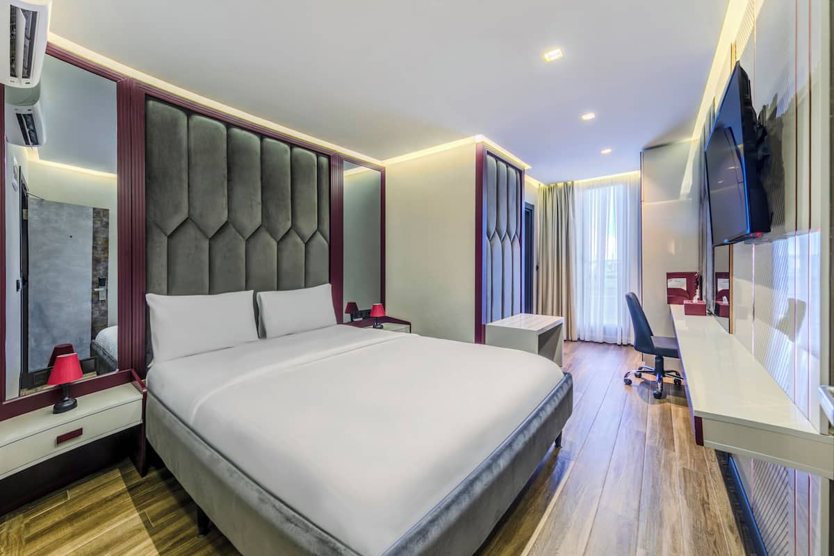 A modern hotel room with a large bed, a desk, a TV, and a mirror.