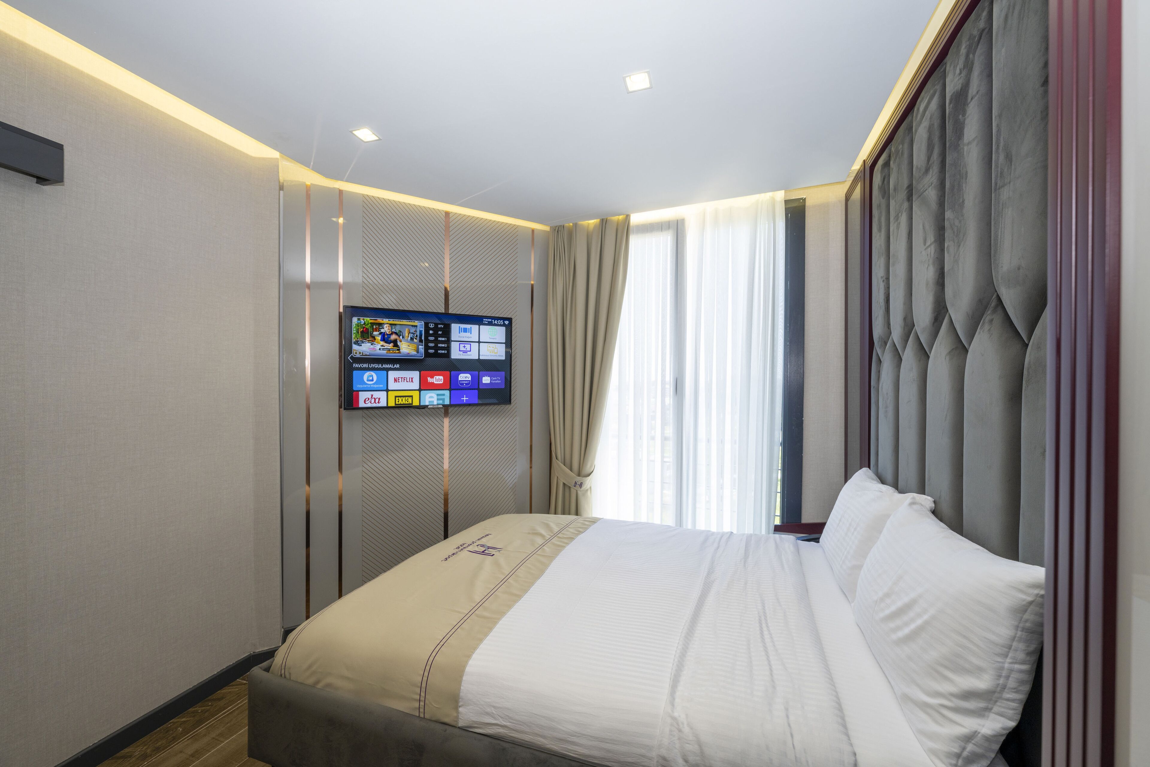 Una moderna camera d'albergo con un letto grande, una TV a schermo piatto montata a parete e una finestra con tende.