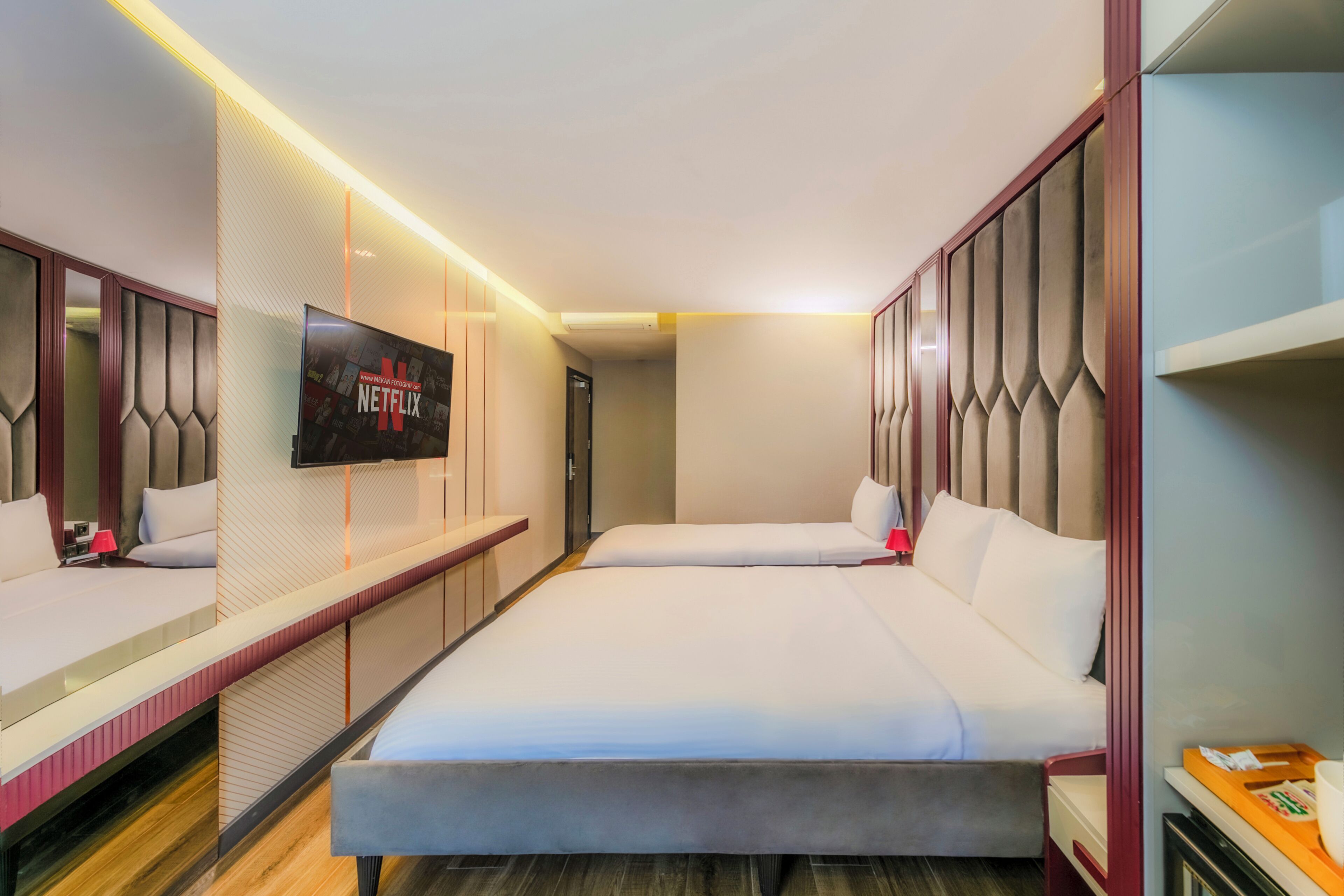 Camera d'albergo con due letti, una televisione montata a parete e un armadio in legno.