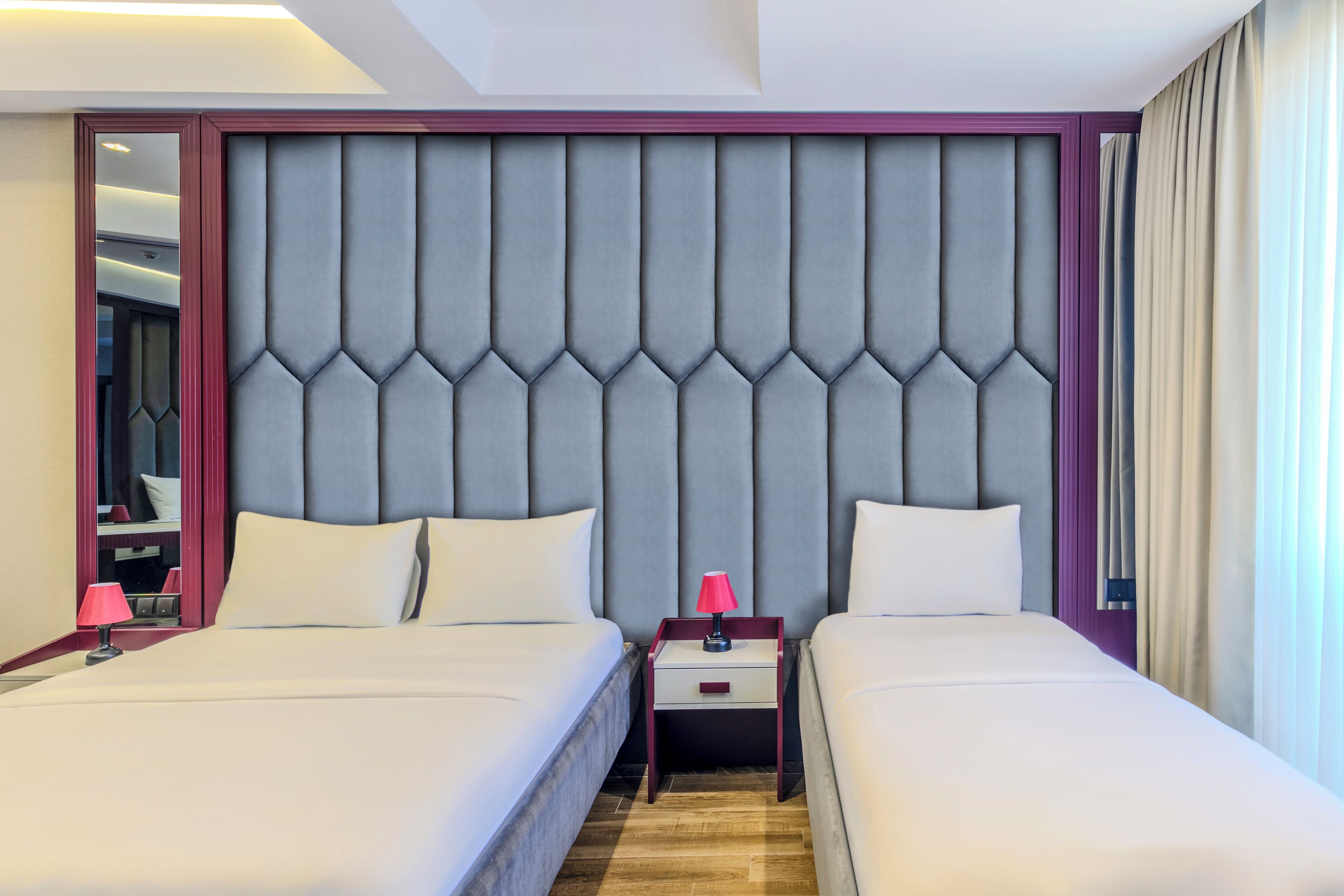 Una habitación de hotel con dos camas, un cabecero con diseño geométrico, una mesita de noche con lámpara y un espejo.