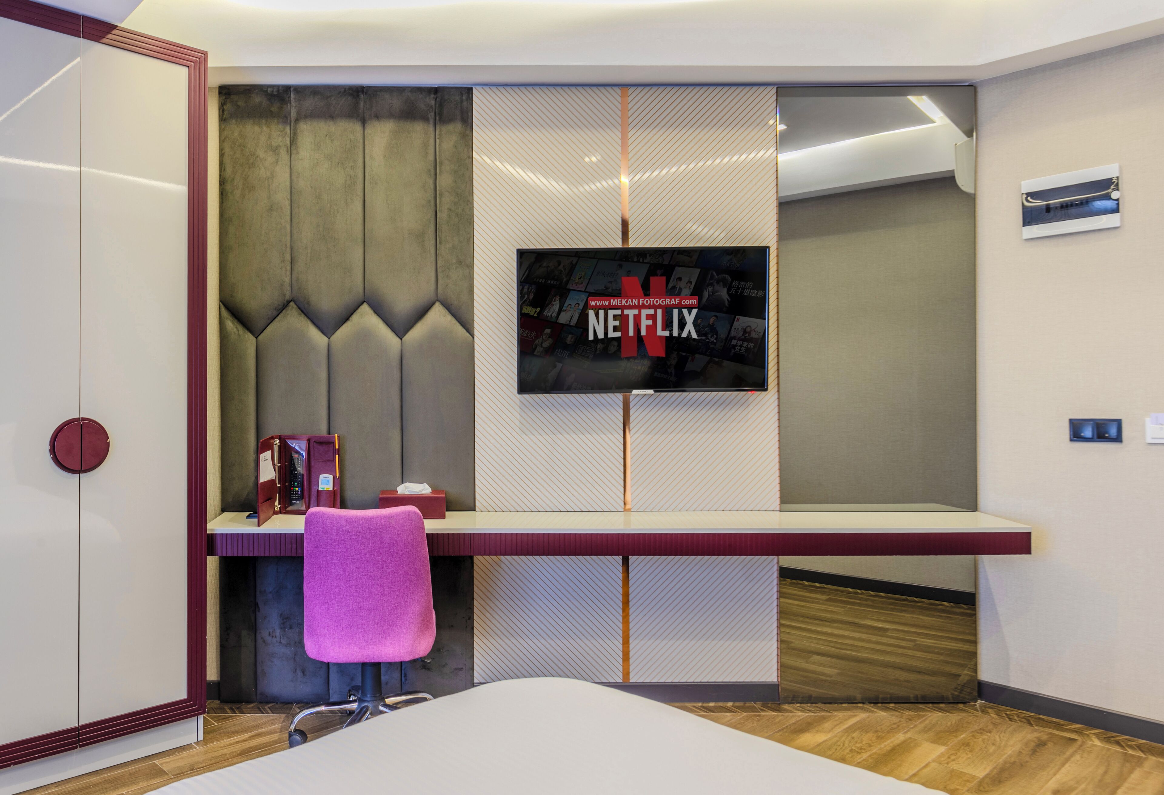 Una habitación moderna con una televisión de pantalla plana grande montada en una pared texturizada, un escritorio con una silla y un armario.