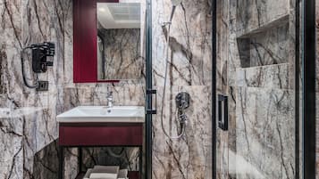 Un baño moderno con ducha de vidrio, pared de mármol, suelo de madera y tocador rojo.