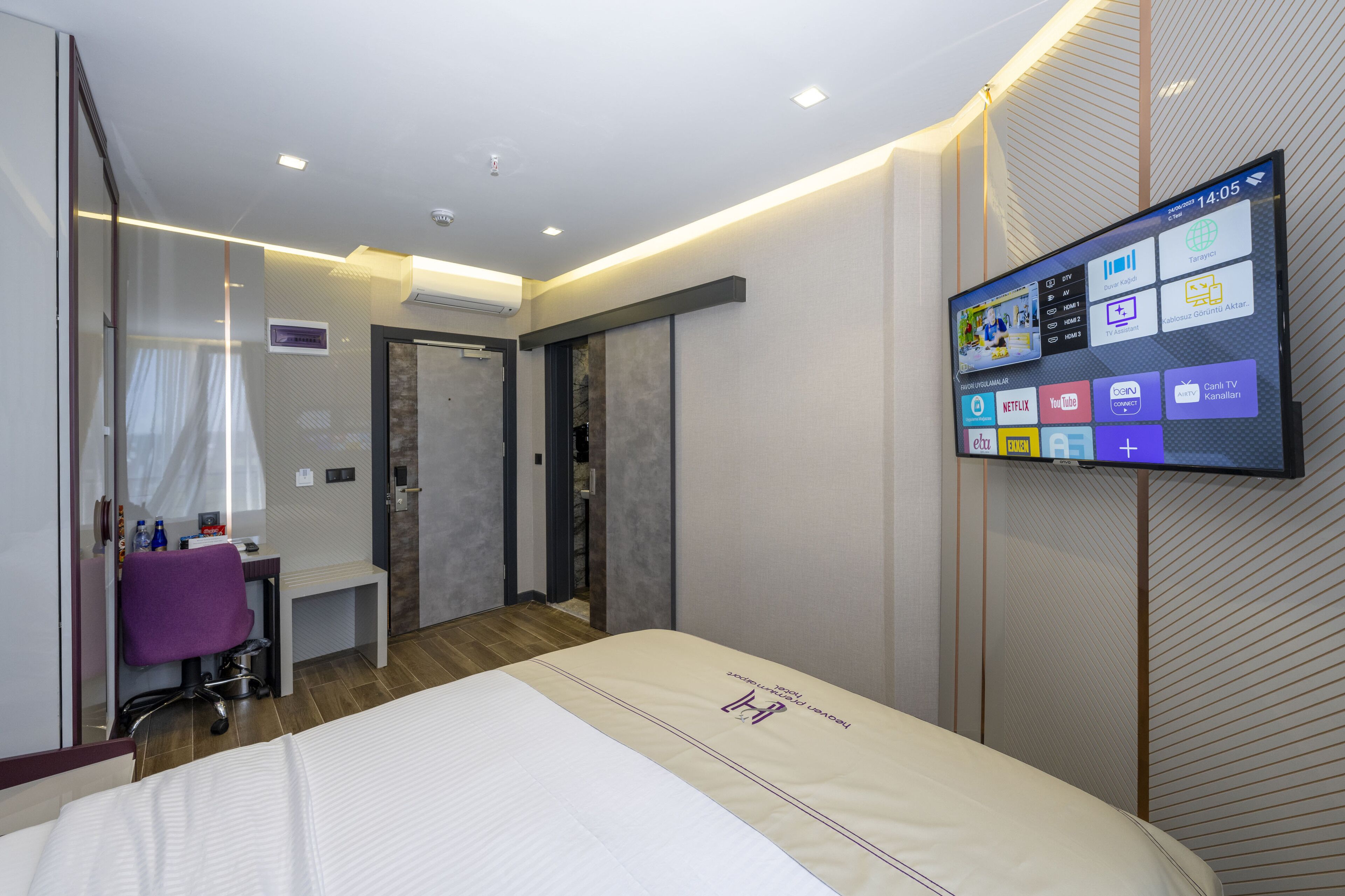 Ein modernes Hotelzimmer mit Bett, Schreibtisch, Sessel, Fernseher und Badezimmer.