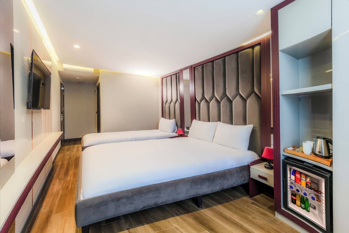 A modern hotel room with a large bed, a television mounted on the wall, and a minibar with beverages.