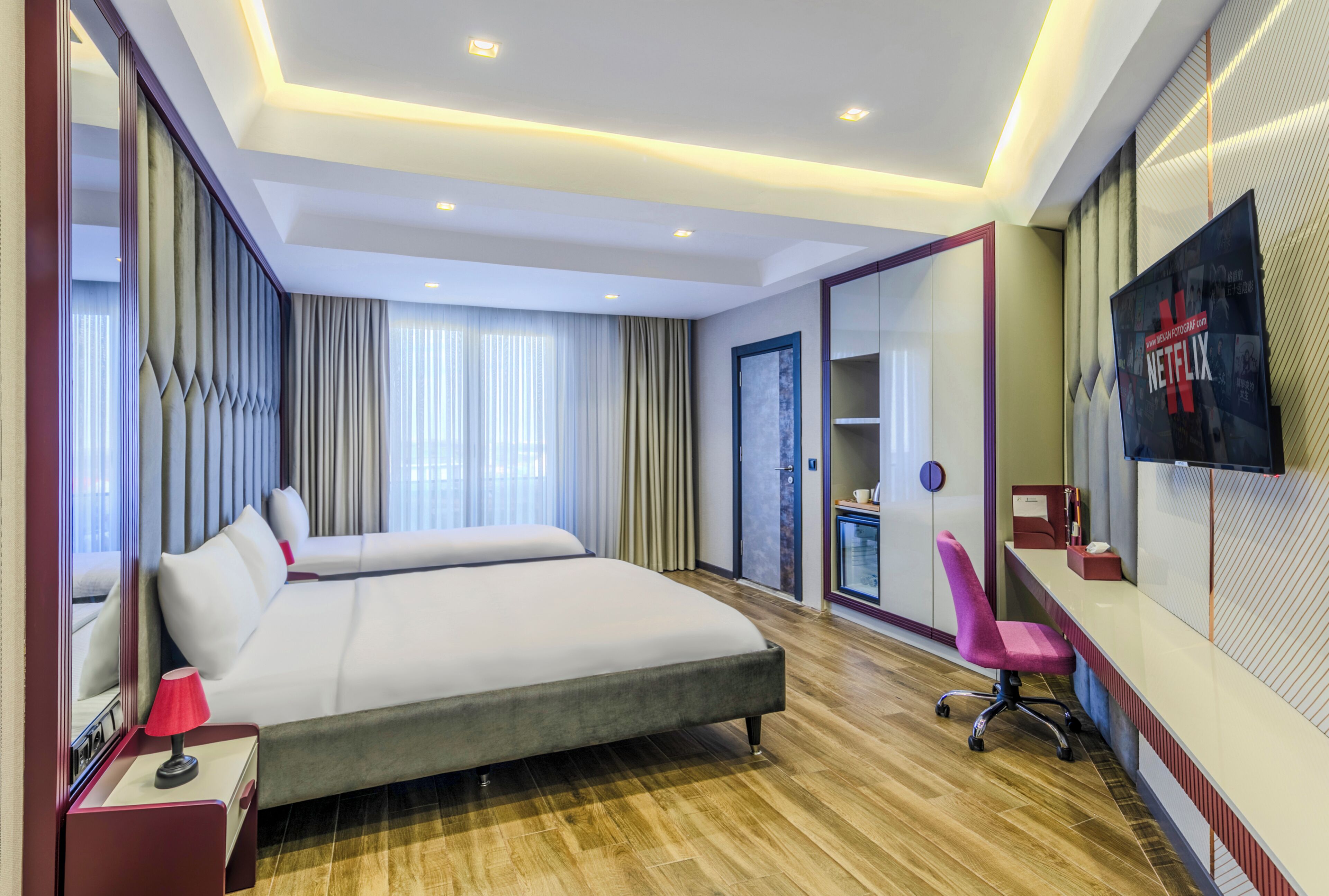 A modern hotel room with a large bed, a desk with a chair, a TV, and a large mirror.