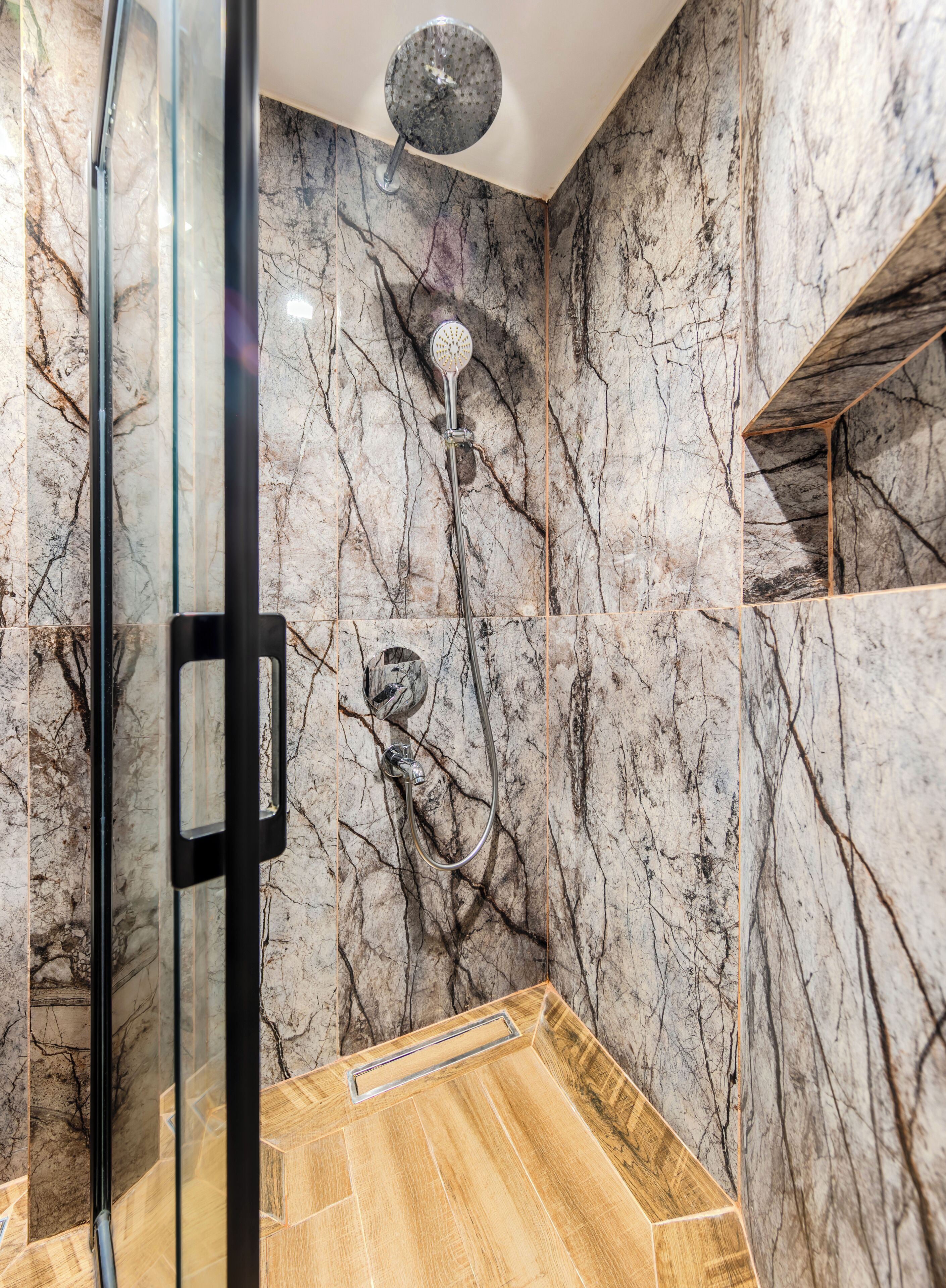 Une salle de bain moderne avec une douche à parois de verre, des murs en marbre et un plancher en bois.