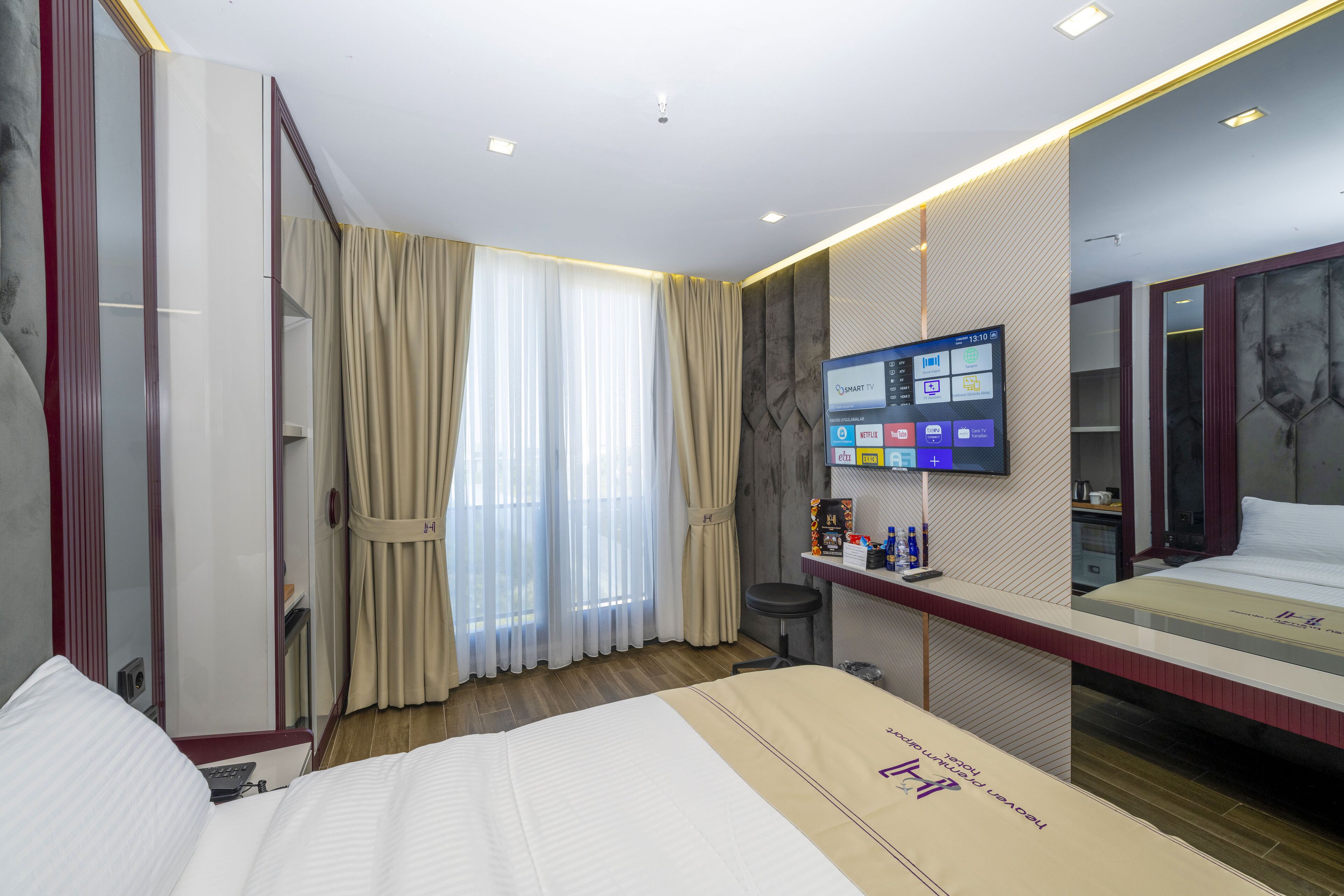 A hotel room with a large bed, a TV mounted on the wall, a desk with a chair, and a mirror.