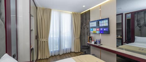A hotel room with a large bed, a TV mounted on the wall, a desk with a chair, and a mirror.