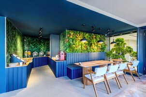 Un área de comedor moderna con una paleta de colores azul y verde, que presenta una larga barra con bufé y un espacio de estar con mesas y sillas de madera.