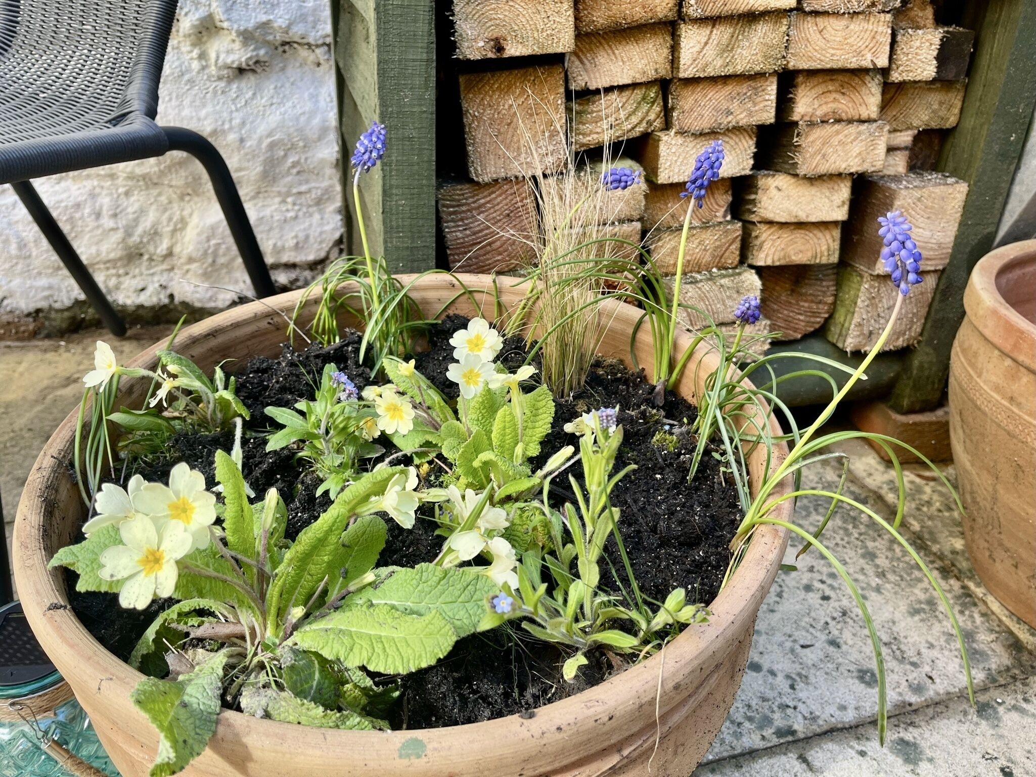 A wooden planter with various plants and flowers, placed on a concrete surface.