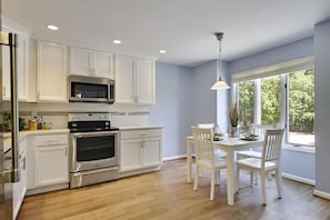 A modern kitchen with white cabinets, stainless steel appliances, and a dining area with white chairs and a table. - 3 Bedroom 2.5 bath end unit Townhome in The Salt Pond Community near Bethany Beach (Bethany Beach)
