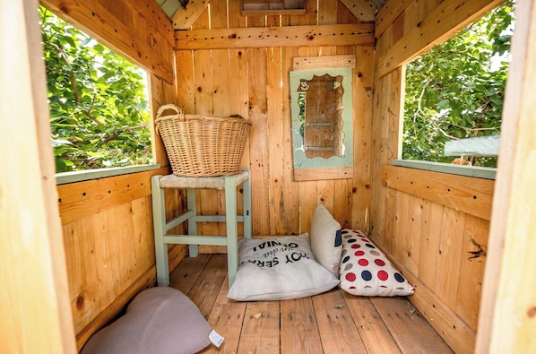 Quarto de cabana de madeira aconchegante com um cesto de vime sobre um banquinho, uma almofada com texto e uma almofada de bolinhas.
