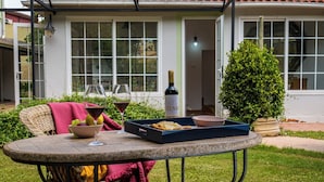 An outdoor dining area with wicker furniture, a table with a bottle of wine, glasses, and a tray with food.