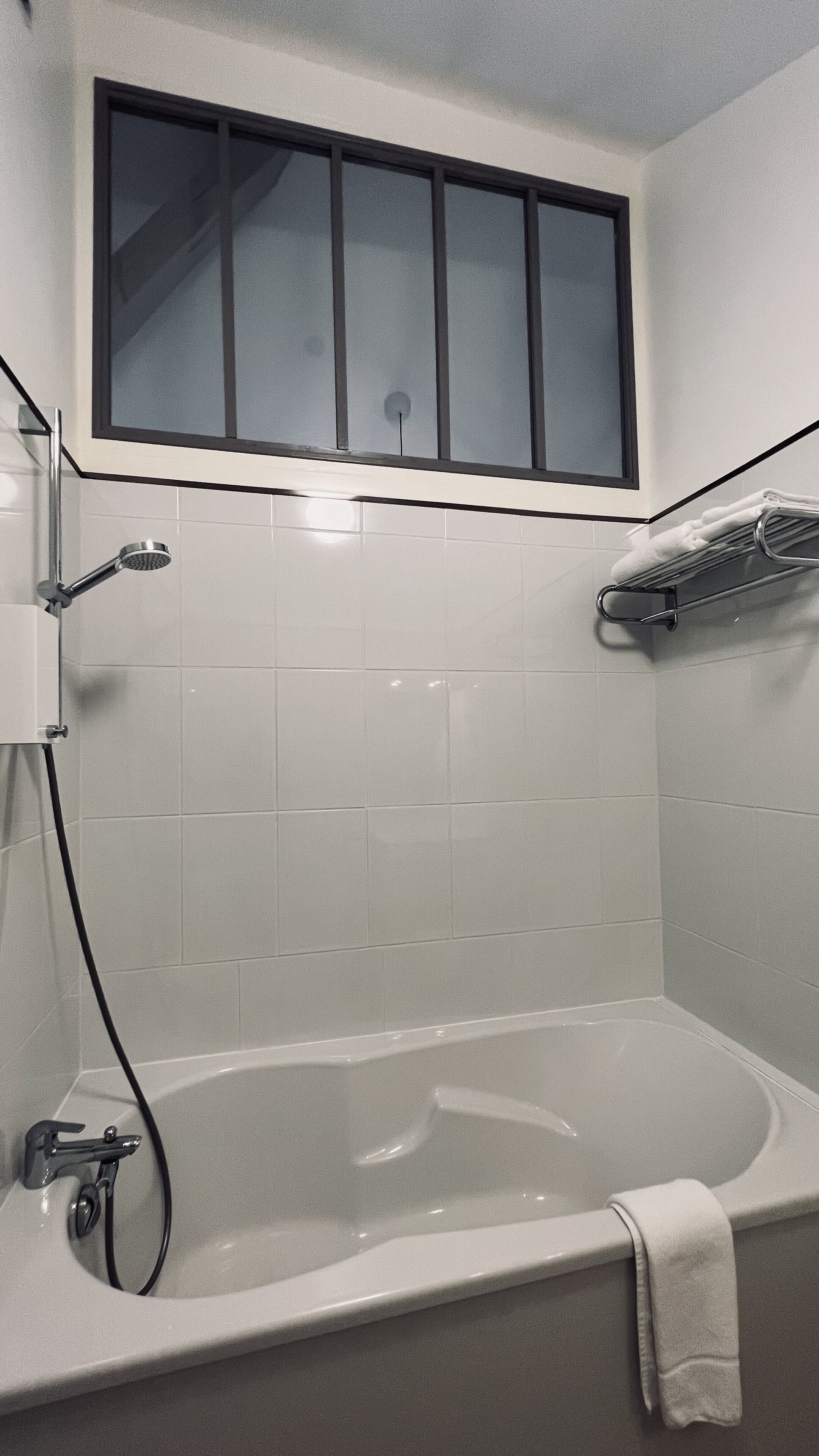 Un baño con bañera, una ventana sobre la bañera y un perchero para toallas.