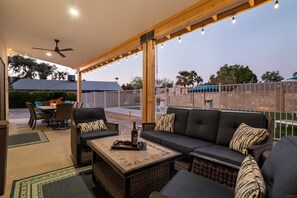 Un patio couvert comprenant un canapé, une table à manger et des chaises, agrémenté d’un ventilateur de plafond et de guirlandes lumineuses.